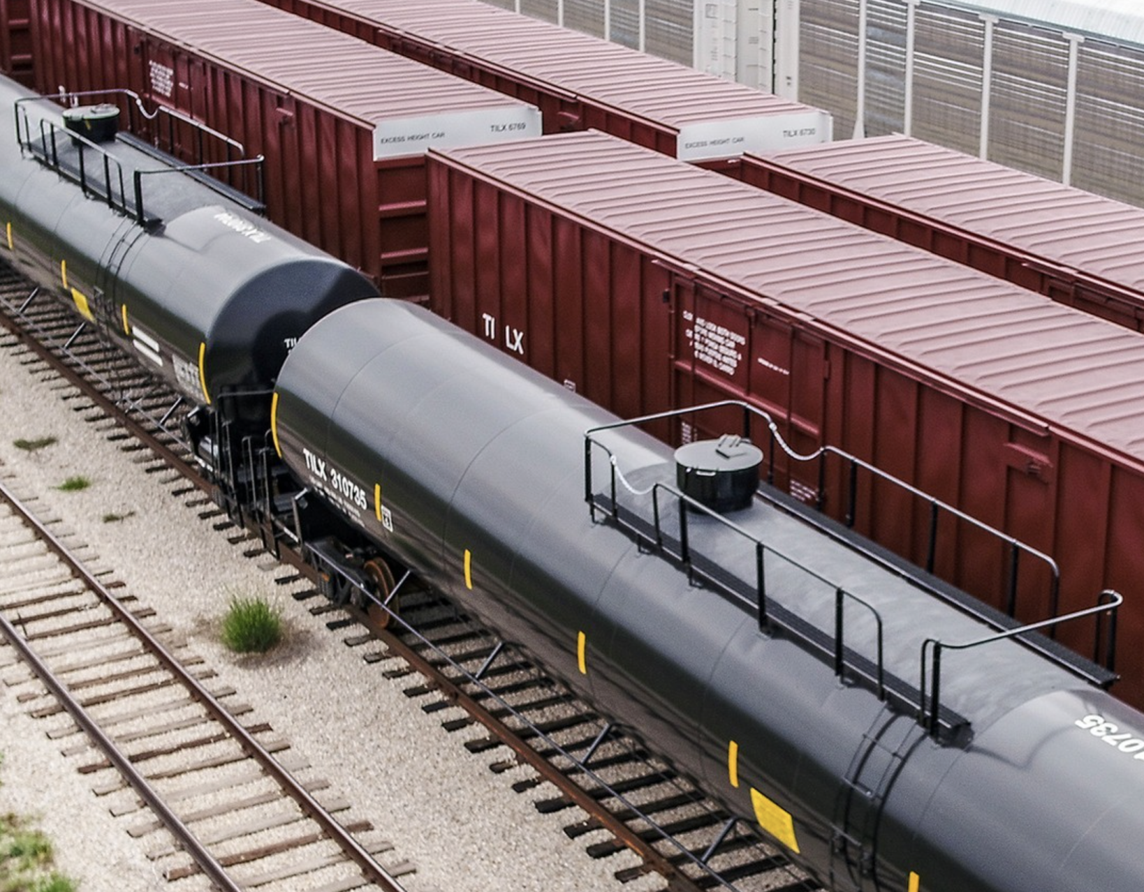 Lines of black tank cars and red box cars sit side-by-side on a track