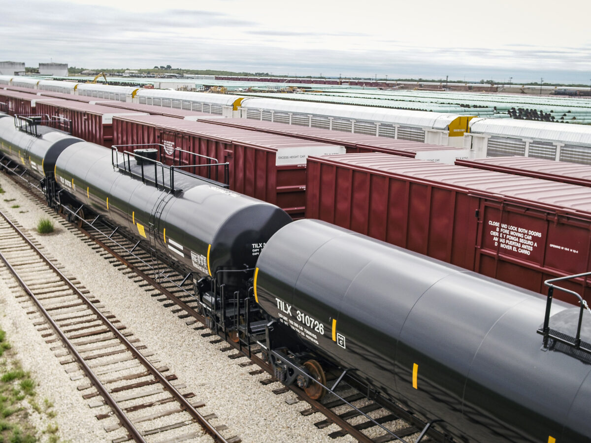 Various types of railcars, including tank cars and box cars, line a railyard